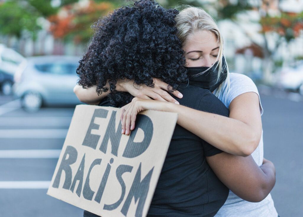 Zwei Frauen liegen sich in den Armen, auf einem Demo-Plakat steht "End Racism"